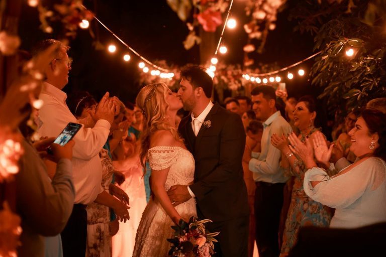 Couple shares a tender kiss surrounded by friends at a romantic outdoor wedding at night.