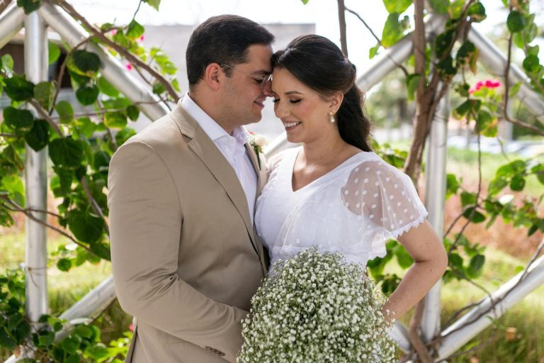 Bride and groom smiling and embracing in a lush garden setting on their wedding day.